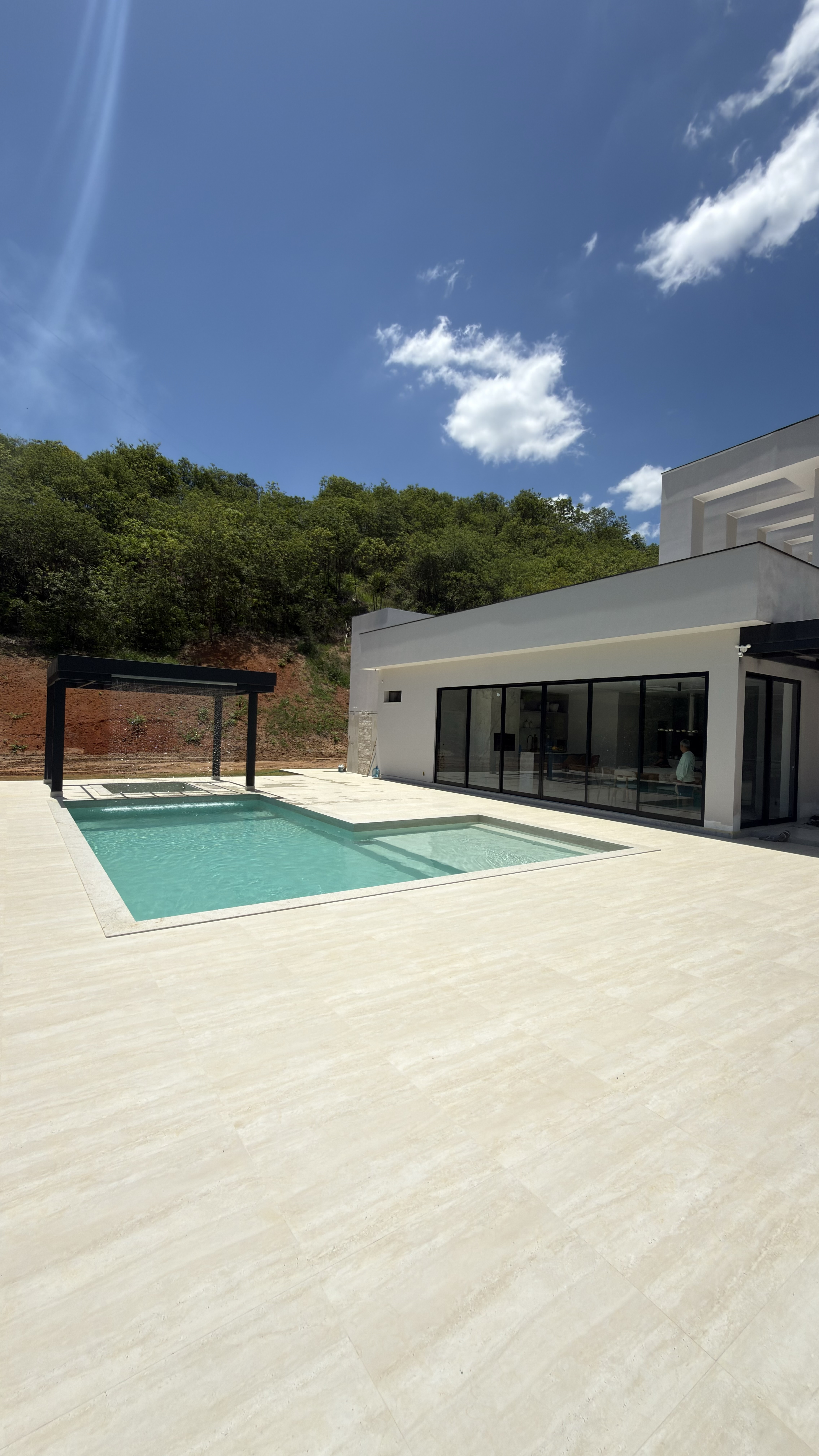 Piscina de alvenaria com porcelanato bege, pérgola e prainha, integrada à casa de alto padrão