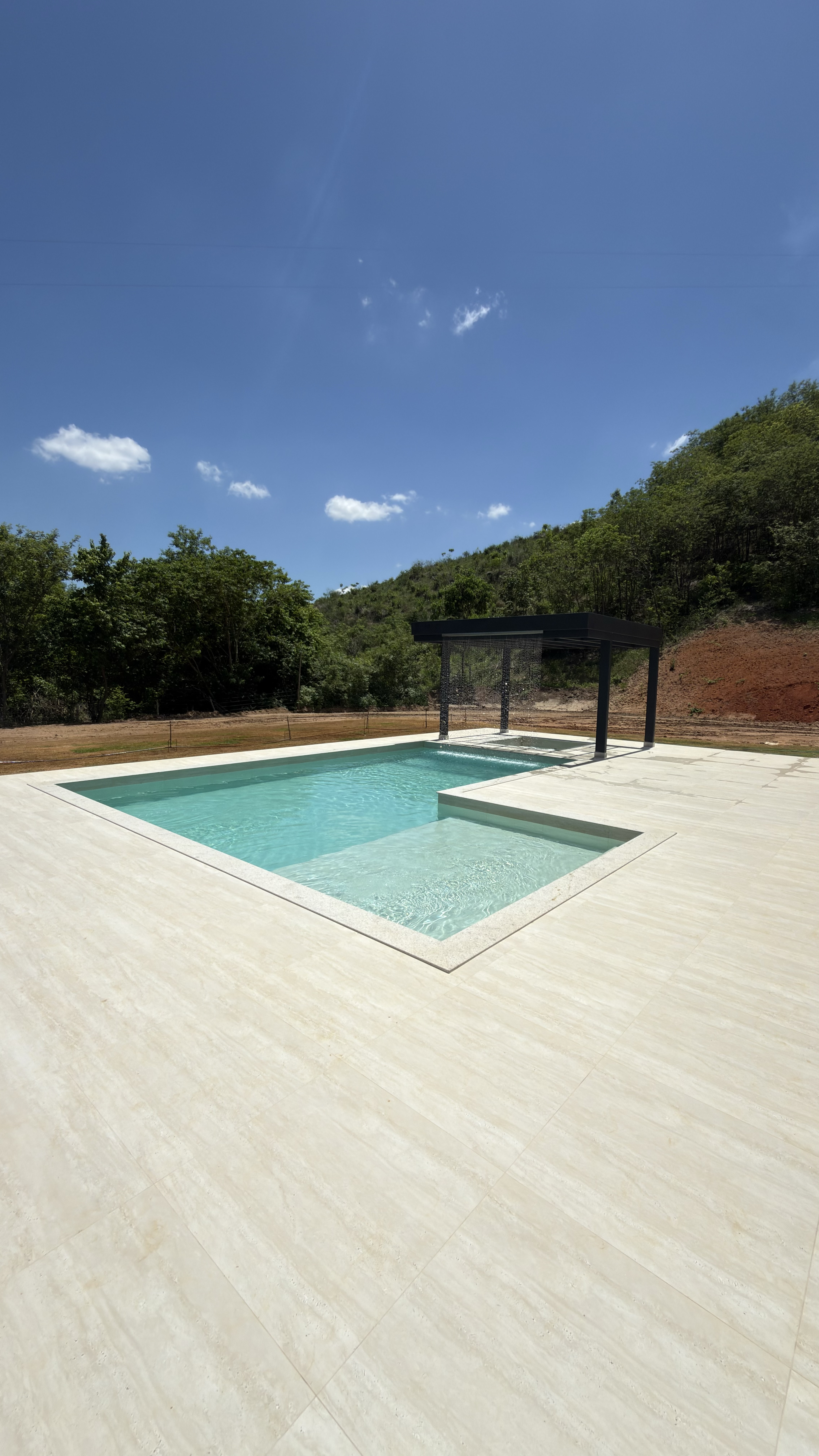 Piscina de alvenaria em porcelanato estrutural com deck amplo e pérgola